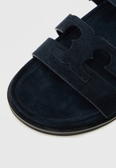 Marineblå ruskinds slide-sandal med to brede stropper med udskæringer. Flad sål med sorte accenter og en struktureret fodseng.