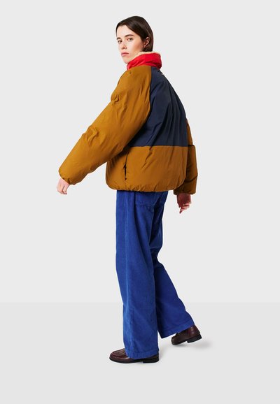 Giacca a vento imbottita con corpo marrone, retro blu navy e colletto rosso. Il design presenta maniche larghe e una finitura trapuntata e texturizzata.