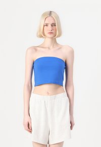 Blå strapless crop top i mjukt tyg, parat med ljusgrå shorts med elastisk midja. Slät textur, åtsittande stil och minimalistisk design.