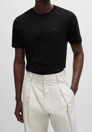 Schwarzes Baumwoll-T-Shirt mit Rundhalsausschnitt und kleinem "BOSS"-Logo auf der Brust, kombiniert mit kremfarbigen, hoch taillierten, plissierten Hosen.