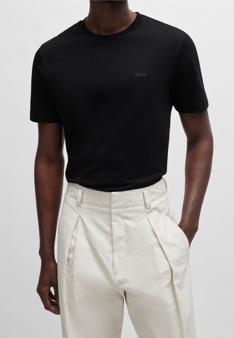Černé bavlněné tričko s kulatým výstřihem a malým logem "BOSS" na hrudi, spárované s krémovými, vysoko pasovými plisovanými kalhotami.