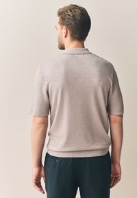 Polo à manches courtes gris clair avec un motif texturé sur les épaules et un corps uni, col et ourlet côtelés.