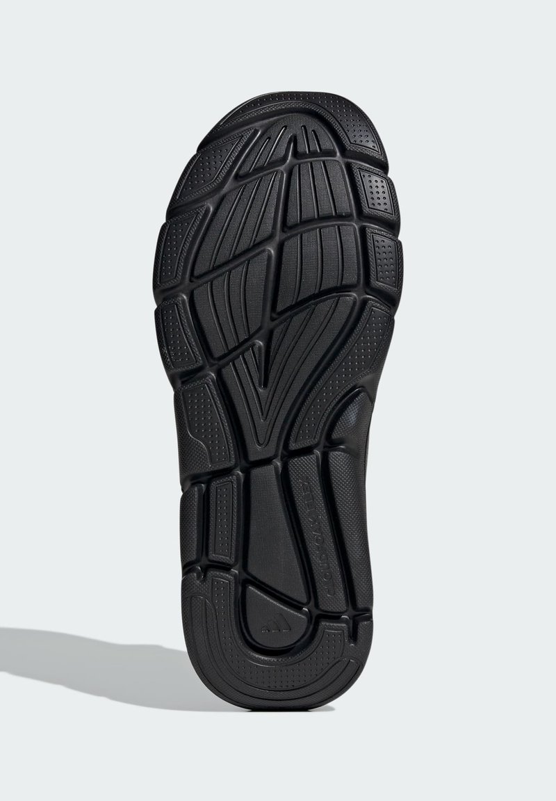 Semelle de chaussure en caoutchouc noir présentant un design texturé avec des rainures, des motifs et un logo central. Bande de roulement détaillée pour une meilleure traction.