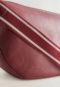Bolso de hombro de cuero burdeos con una superficie texturizada, que presenta una correa trenzada con rayas crema. Forma redondeada con costuras visibles.