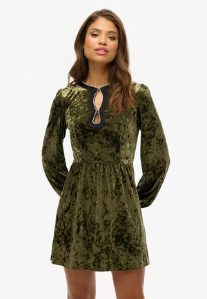 Olive green velvet dress with long sleeves, keyhole neckline, black trim, and a flared skirt. Features textured fabric and decorative detailing.