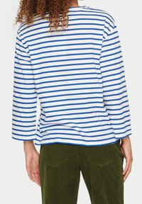 Pasiasty longsleeve z niebieskimi i białymi paskami; luźny krój z okrągłym dekoltem; zestawiony z oliwkowozielonymi spodniami z kordurowej tkaniny.