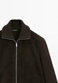 Giacca di un marrone scuro, con cerniera, colletto e maniche a coste; corpo in morbido suede con tasche laterali; design minimalista.