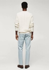 Weißer, kabelgestrickter Pullover mit Rundhalsausschnitt, kombiniert mit hellblauen Jeans und braunen Lederschuhen. Standardpassform, Ansicht von hinten.