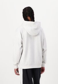 Sudadera con capucha de color gris claro, de corte holgado, mangas largas y puños acanalados. Textura suave, costuras visibles y detalle de costura en la parte posterior.