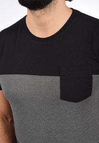 Černé a šedé tričko s krátkým rukávem, kulatým výstřihem a horizontálním designem s bloky barev, s náprsní kapsou ve shodné černé látce.