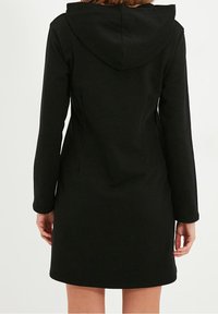 Svart huva kappa med långa ärmar, slim fit, midje-längd, och en slät textur. Har en enkel, ren design.