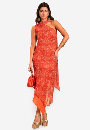 Vestido naranja asimétrico con tejido estampado, un hombro, y una textura suave y fluida, combinado con un bolso naranja y tacones de plataforma dorados.