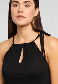 Top negro tipo halter con corte en forma de ojal, tela fruncida en el escote y cintas ajustables en los hombros para un ajuste personalizable.