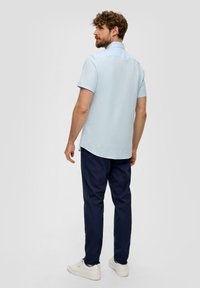 Lichtblauw overhemd met korte mouwen en een kraag, zachte textuur, en een rechte zoom, gecombineerd met marineblauwe broek en witte sneakers.