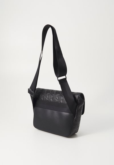 Sac en bandoulière noir avec un dessus texturé à motifs en losanges, une section inférieure lisse et une large bandoulière réglable.