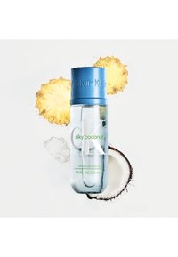 Flacon pulvérisateur transparent avec un couvercle bleu, étiqueté "CK Silky Coconut," affichant un design minimaliste et entouré de tranches de noix de coco et d'ananas.