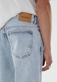 Světle modré džíny z denimu s volným střihem, s béžovou koženou cedulkou s ražbou "PULL&BEAR" a dvěma zadními kapsami s šitými detaily.