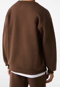 Hnědá mikina vyrobená z měkké tkaniny, s volným střihem, kulatým výstřihem a žebrovanými manžetami a spodním lemem. Minimalistický design bez vzorů.