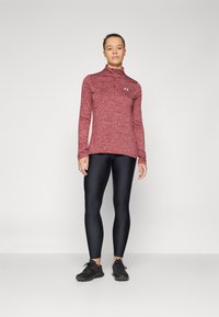 Rød lyng langærmet top med en kvart lynlås, parret med sorte leggings. Modellen bærer sorte træningssko.