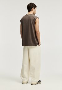 Ruskea hihaton t-paita raidoilla, yhdistettynä löysiin off-white-housuihin ja mustiin lenkkikenkiin, nähtynä takaa.