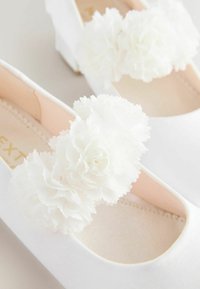 White satin flats with floral fabric accents, featuring three-dimensional white flower embellishments, rounded toe, and soft beige insole.
