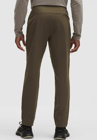 Oliwkowozielone, lekkie spodnie o gładkiej fakturze, z elastycznym pasem i zwężanymi nogawkami, zestawione z czarnymi butami sportowymi.