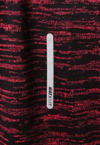 Tela de patrón negro y rojo con una textura suave presenta una etiqueta blanca vertical que dice "NIKE". Los patrones tienen un diseño en forma de ola.