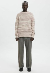 Maglione a righe rosa chiaro e crema con scollo tondo, abbinato a pantaloni grigi plissettati e scarpe nere. Tessuto liscio, vestibilità comoda.