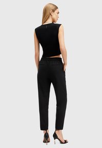Top nero senza maniche e cropped abbinato a pantaloni neri a gamba affusolata, con vita elastica e tasche laterali. Indossato con tacchi neri.