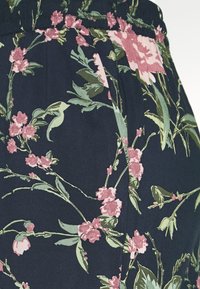 Tmavě modrá látka s květinovým vzorem zahrnujícím růžové květy a zelené listy. Pas je elastický, což vytváří přiléhavý tvar.