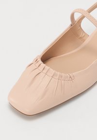 Chaussure plate en cuir rose pâle avec un bout carré, présentant des détails froncés autour de l'ouverture et une petite lanière pour le soutien.