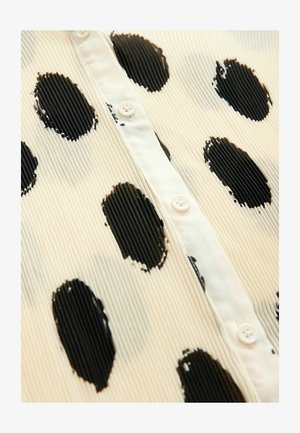 Biała koszula w czarne kropki, z teksturowanej tkaniny, z zapięciem na guziki, prezentująca pionowe zakładki i gładkie akcenty.