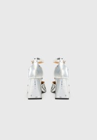 Ασημί ψηλά παπούτσια με φαρδύ τακούνι και λουράκι στον αστράγαλο. Λείο, γυαλιστερό υλικό με απαλή υφή, με σχέδιο στρογγυλής μύτης.