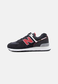 Μαύρο και κόκκινο αθλητικό παπούτσι New Balance με λευκή ενδιάμεση σόλα, ετικέτα από ύφασμα Cordura και υφασμένη λαστιχένια εξωτερική σόλα, εμφανιζόμενο σε προφίλ δεξιάς πλευράς πάνω σε λευκό φόντο.