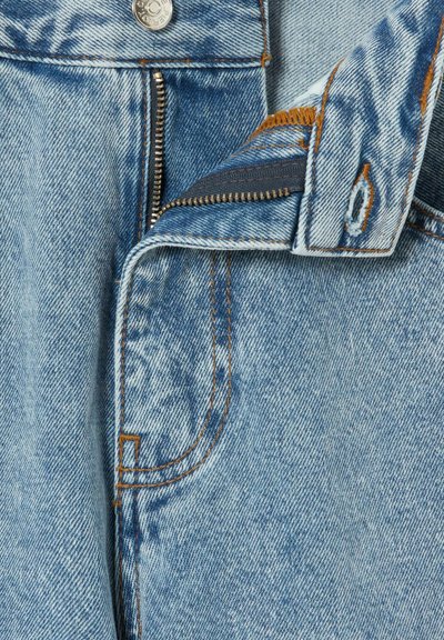 Jeans in denim azzurro chiaro con cerniera, bottone argento e cuciture arancioni. Vista ravvicinata che mette in evidenza la trama del tessuto e il design della tasca.