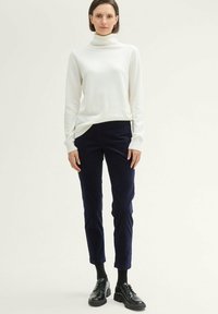 Witte coltrui met een zachte textuur, gecombineerd met donkerblauwe slim-fit corduroybroek. Zwarte veterschoenen maken de outfit compleet.