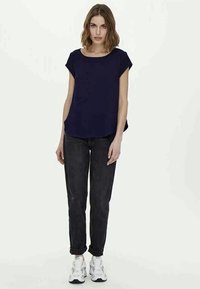 Marineblaue Kurzarmbluse mit Rundhalsausschnitt, kombiniert mit dunkler Jeans und weißen Sneakern. Lässiger Schnitt mit entspanntem Design.