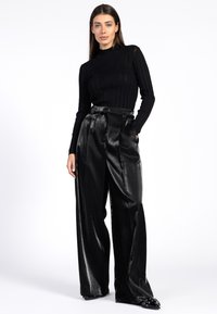 Zwarte geribbelde turtleneck trui gecombineerd met hooggetailleerde, glanzende zwarte wijde broek. Zachte textuur, stijlvolle ontwerp en op maat gemaakte pasvorm.