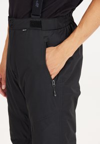 Zwarte skibroek met verstelbare bretels, twee zijzakken met rits en een klittenbandsluiting bij de tailleband. Gemaakt van duurzaam materiaal.