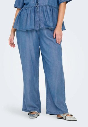 Jeans top met een peplum zoom, gecombineerd met wijde jeans broeken. Beide zijn in een middelblauwe tint. Schoenen hebben zilveren accenten.