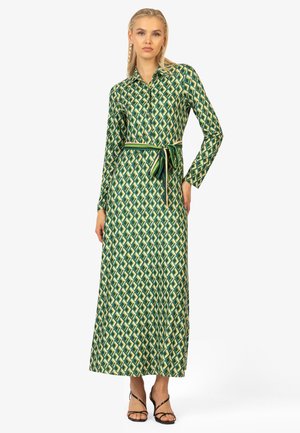 Maxi-Kleid aus grünem Stoff mit einem geometrischen Muster aus Rauten und Quadraten. Lange Ärmel, Knopfleiste und passender Gürtel.