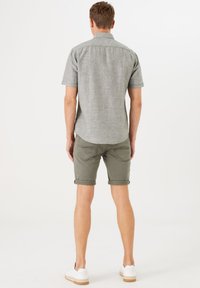 Camisa de manga corta gris claro, de tela texturizada; pantalones cortos verde oliva, enrollados; zapatillas blancas con suela marrón clara.