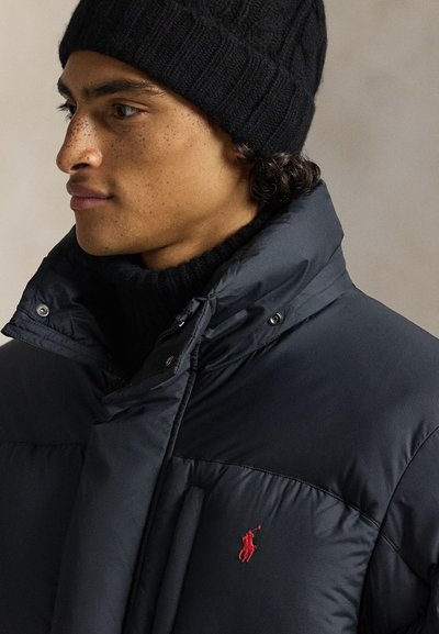 Μπουφάν navy με καπιτονέ σχέδιο, διαθέτει ψηλό γιακά, κουμπώματα με τρουκ και κόκκινο κεντημένο λογότυπο στο στήθος. Φορά μαύρ�ο πλεκτό σκουφάκι.