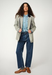 A gray textured blazer with black lapels, a blue patterned button-up shirt, wide-leg blue jeans, and woven brown shoes.