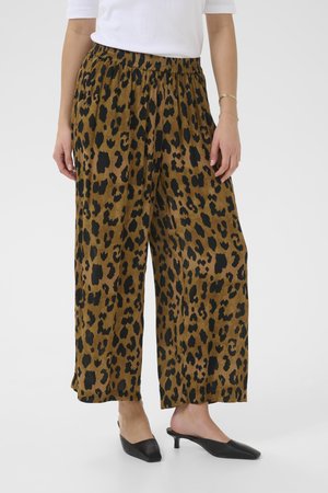 Pantalons marron à jambes larges avec un imprimé léopard noir, dotés d'une taille élastique. Associés à des chaussures noires à bout pointu.