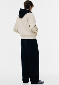 Beige hættetrøje med sort hætte, blanding af bomuldsstof, løs pasform, elastiske manchetter og talje. Parret med sorte brede sweatpants med lommer.
