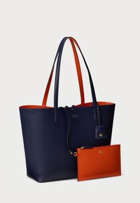 Πετρώδη δερμάτινη τσάντα σε ναυτικό μπλε με πορτοκαλί λεπτομέρειες, διαθέτοντας μακριές λαβές και αποσπώμενη πορτοκαλί �θήκη με χρυσά αξεσουάρ.