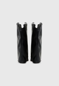 Botas de tobillo negras de cuero con un acabado texturizado, que presentan una silueta única y dos tiradores laterales para facilitar su uso.