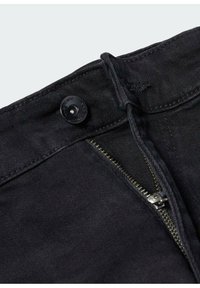 Jean en denim noir avec fermeture éclair à l'avant, quincaillerie en métal argenté et bouton noir assorti. Tissu texturé avec une finition lisse.