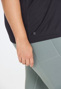 Sort atletisk t-shirt med en glat tekstur, der har et lille logo-detalje. Parret med tætsiddende, lysegrå leggings med sømdetaljer.